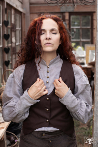 La créatrice Maureen Vinoten veston en laine marron et chemise en lin gris boutonnée.
Femme aux cheveux roux bouclés qui ferme les yeux et qui porte un veston boutonné en laine marron