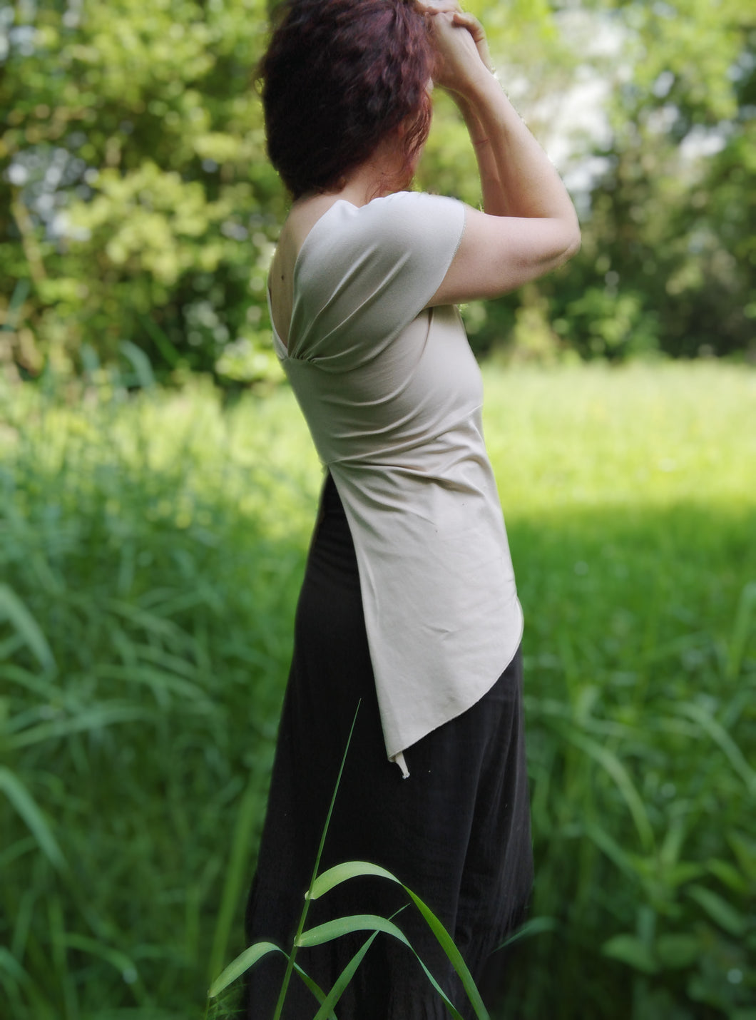 femme debout dans une prairie aux herbes hautes, elle porte un tee shirt en jersey beige. Ses cheveux auburn sont tressés.
Création Maureen Vinot