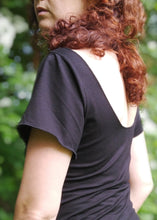 Charger l&#39;image dans la galerie, créatrice Maureen Vinot, portant un tee shirt noir à manche courtes et dos nu arrondi, dans une forêt.