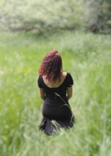 Charger l&#39;image dans la galerie, femme assise dans une prairie verdoyante, habillée avec un tee shirt dos nu noir et une jupe noire. Création Maureen Vinot