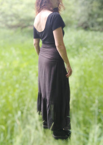 femme debout dans une prairie verdoyante, habillée avec un tee shirt dos nu noir et une jupe noire. Création Maureen Vinot