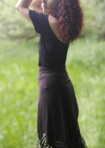 femme dans une prairie verdoyante, habillée avec un tee shirt dos nu noir et une jupe noire. Création Maureen Vinot