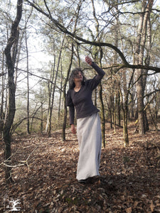 femme qui marche dans la forêt et habillée d'une longue jupe de lin fluide. D'un pull beige à manches bouffantes. Ces vêtements sont ceux de la créatrice Maureen. Ils sont fabriqués en Bretagne