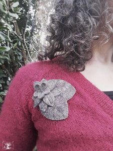 broche en feutre gris naturel chiné portée sur un gilet rouge. La broche est composée de deux feuilles nervurées et d'une grande fleur, créatrice Maureen , fabriqué en Bretagne
